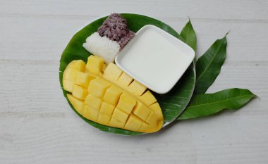 Lezzetli Tayland mango yapışkan pirinci taze ve olgun mango meyvesi seramik bir tabakta ahşap bir masa üzerinde izole edilmiş. Yaz zamanı Tayland tatlısı. Glutinous rice, mango, hindistan cevizi sütü.