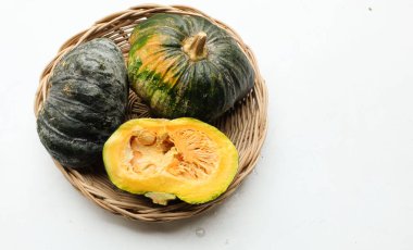 Bir yığın taze çiğ Japon balkabağı (Cucurbita moschata), Kabocha kabağı, beyaz bir arka planda izole edilmiş bir hasır sepet içinde. Sağlıklı gıda sebze, meyve ve gıda ticareti fikri