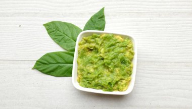 Avokado kreması, avokado sosu, avokado sosu, avokado sosu, seramik kâse ve avokado dilimleriyle servis edilen yarım yamalak diyet beyaz ahşap zemin üzerinde izole edilmiş.