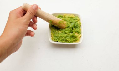 Kadın Asyalı taze yeşil Avocado 'yu beyaz bir arka planda izole edilmiş küçük bir seramik kasede ezdi. Sağlıklı bebek maması, sebze ve meyve fikirleri.