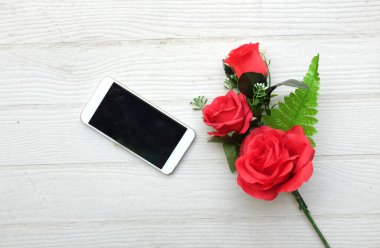 Güzel kırmızı gül buketi, çiçek ve cep telefonu, ahşap zemin üzerindeki akıllı telefon fotokopi alanı veya metin, afiş, hediye, Sevgililer Günü kutlamaları.