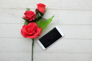 Güzel kırmızı gül buketi, çiçek ve cep telefonu, ahşap zemin üzerindeki akıllı telefon fotokopi alanı veya metin, afiş, hediye, Sevgililer Günü kutlamaları.