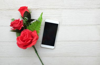 Güzel kırmızı gül buketi, çiçek ve cep telefonu, ahşap zemin üzerindeki akıllı telefon fotokopi alanı veya metin, afiş, hediye, Sevgililer Günü kutlamaları.