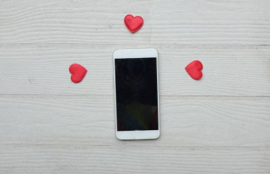 Küçük kırmızı kalplerle çevrili siyah bir akıllı telefon beyaz bir arkaplanda izole edilir. Sosyal medya ve dijital pazarlama, Sevgililer Günü, Teknoloji, Özel Yıl dönümü konsepti.