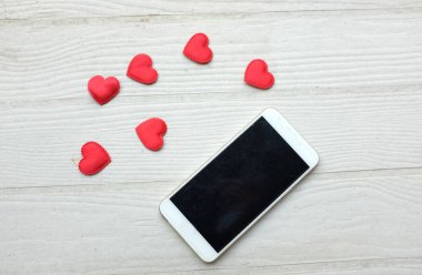 Küçük kırmızı kalplerle çevrili siyah bir akıllı telefon beyaz bir arkaplanda izole edilir. Sosyal medya ve dijital pazarlama, Sevgililer Günü, Teknoloji, Özel Yıl dönümü konsepti.