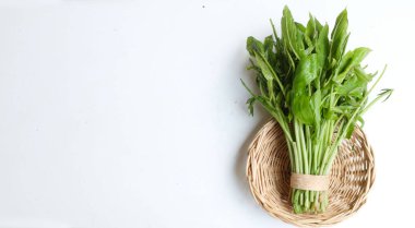 Tahta bir sepetin içinde taze çiğ bir demet (Lasia spinosa) beyaz bir arka planda izole. Taze yapraklı yeşil sebze. Asya malzemesi. Sağlıklı vejetaryen yemekleri