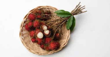 Olgun kırmızı rambutanlar (Nephelyum Lappaceum) bütün ve yarım ve yeşil yapraklı ahşap bir sepetin içinde beyaz bir arka planda izole edilmiş bir meyvedir. Rambutan kırmızı kabuklu, beyaz etli, kahverengi tohumlu bir meyvedir. Şekeri var. 