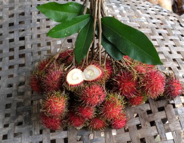 Taze olgun kırmızı rambutanları (Nephelyum Lappaceum) bir bütün ve yeşil yaprakları beyaz bir arka planda izole eder. Rambutan kırmızı kabuklu, beyaz etli, kahverengi tohumlu bir meyvedir. Tatlı bir tadı var.,