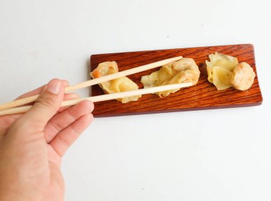 Shumai ya da Çin Buharlı Hamur köftesi, Wonton derili köfte yemek için çubuk kullanan kadın, soya soslu ahşap bir tabakta servis ediliyor, yemek çubukları beyaz bir zeminde izole ediliyor.