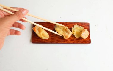 Shumai ya da Çin Buharlı Hamur köftesi, Wonton derili köfte yemek için çubuk kullanan kadın, soya soslu ahşap bir tabakta servis ediliyor, yemek çubukları beyaz bir zeminde izole ediliyor.