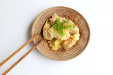 Buharda Shumai ya da Çin Buharlı Hamur köftesi, Wonton derili köfte yemek için çubuk kullanan kadın, buharda pişirilmiş domuz etli börek, beyaz bir zeminde izole edilmiş ahşap bir tabakta servis ediliyor.