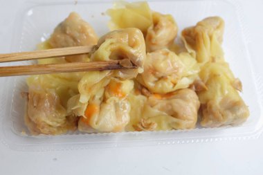 Shumai, Siu Mai 'de yemek çubuğu kullanan bir kadın, Çin buğulanmış hamur köftesi, soya soslu şeffaf plastik bir kutuda, beyaz bir zemin üzerinde izole edilmiş bir şekilde.