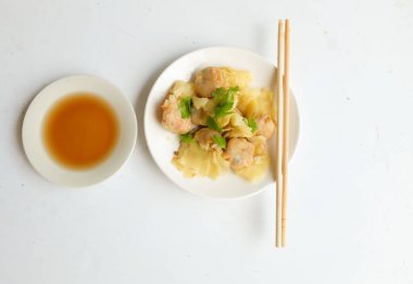 Shumai ya da Çin Buharlı Hamur köftesi, Wonton derili köfte, soya soslu beyaz bir tabakta servis edilen domuz etli börek ve beyaz bir arkaplanda izole edilmiş soya sosu.