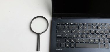 Üst ve düz ofis masasında dizüstü bilgisayarlı klavyesi olan bir büyüteç. konsept çalışma bilgileri internet üzerinden aranıyor .