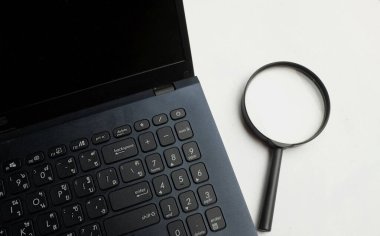 Üst ve düz ofis masasında dizüstü bilgisayarlı klavyesi olan bir büyüteç. konsept çalışma bilgileri internet üzerinden aranıyor .