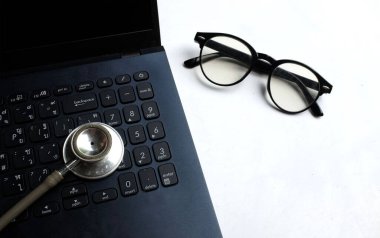 Tıbbi steteskop ve dizüstü bilgisayar, gözlük doktorun masasında. Çevrimiçi tıp, e-sağlık eğitimi, küresel ağ hakkında tıbbi iş raporu. Sağlık ve tıp geçmişi. 
