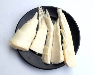 Taze dilimlenmiş ve parçalara ayrılmış bambu filizi, siyah bir plaka içinde bambu filizi (Bambusa spp) beyaz bir arka planda izole edilir. Yer altından kopan yenilebilir bambu. Sebze ve sağlıklı yiyecek.