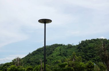 Yeşil doğa dağı ve mavi gökyüzü arka planındaki binanın çatısının altındaki direkte asılı modern bir güneş ışığını kapatın.