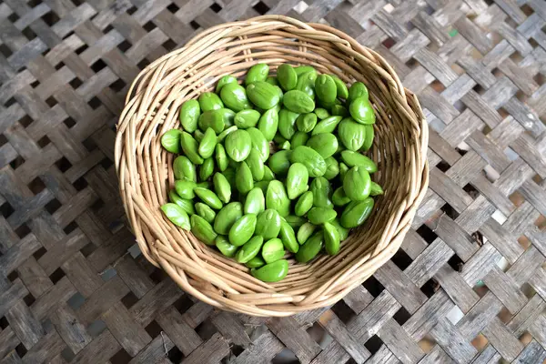 stock image bitter bean, twisted cluster bean, stink bean, sato, petai or pakria,(parkia speciosa) prepare for cooking in a wooden basket isolate on a woven bamboo backdrop .