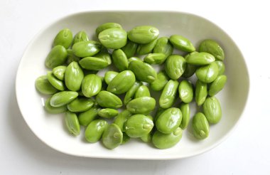 Acı fasulye, bükülmüş fasulye, kokuşmuş fasulye, sato, petai veya pakria, (parkia speciosa) beyaz bir zemin üzerinde beyaz bir tabak içinde pişirmeye hazırlan. Tayland ve Asya malzemeleri için bitkiler .