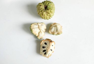 Taze olgun muhallebi, elma şekeri, çeri çiçeği (annona squamosa l.) ile bembeyaz zemin üzerinde izole edilmiş yapraklarla ikiye bölünmüş meyve içeren düz bir kompozisyon. tropikal egzotik meyve