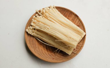 Enoki mantarı (Flammulina filiforis) beyaz bir zemin üzerinde izole edilmiş ahşap bir tabakta bulunur. Vejetaryen ve sağlıklı yaşam tarzı insanları veya sebzeler için besleyici bileşenler