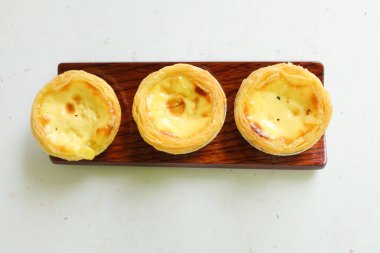 Bir yığın taze yumurta tart tatlı fırında tatlı tatlı pasta ya da Portekiz turtası ahşap tabakta izole edilmiş beyaz bir zemin üzerinde..