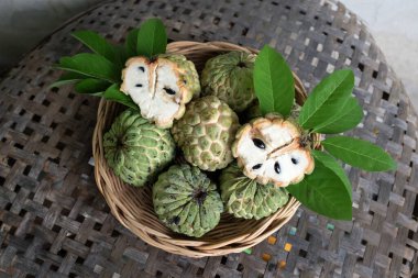 fresh green raw custard apple,sugar apple, annona cherimola (annona squamosa l.) fruit with leaf in a wicker basket on a wooden table backdrop. tropical exotic fruit and healthy fruits clipart