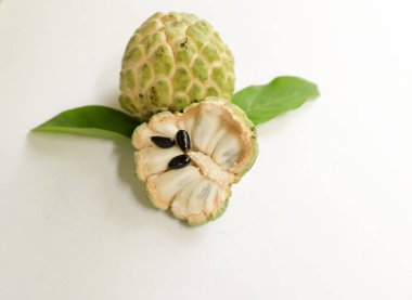 Taze olgun muhallebi, elma şekeri, çeri çiçeği (annona squamosa l.) ile bembeyaz zemin üzerinde izole edilmiş yapraklarla ikiye bölünmüş meyve içeren düz bir kompozisyon. tropikal egzotik meyve