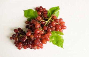 Düz kompozisyon, taze olgun tatlı sulu bütün kırmızı üzümler ve yeşil yapraklar beyaz bir arka planda izole edilmiş. Sağlıklı meyveler.
