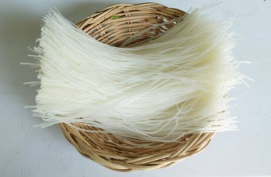 Üst ve düz bir zemin üzerinde kurutulmamış pirinç eriştesi, kurutulmuş çiğ pirinç eriştesi, Tayland kurutulmuş pirinç eriştesi beyaz arka planda izole edilmiş ahtan bir sepetin içinde.