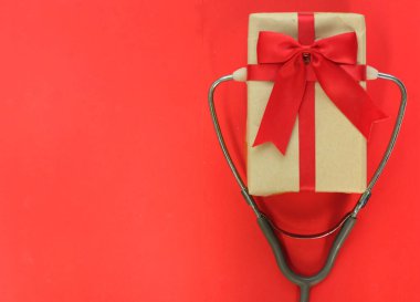 Tıbbî steteskop, dekore edilmiş el yapımı güzel hediye kutusu ve kırmızı kağıttan bir arka plan. Doktorları tebrik etmek için arka plan. Hayat Noel 'i ve yeni yıl tatillerini.