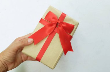 Genç bir kızın elleri, beyaz bir zeminde kırmızı kurdeleli el işi kağıt bir hediye kutusu tutuyor. Enfes bir tebrik konsepti. Yeni yıl hediyeleri, Noel, yeni yıl hediyeleri, Noel, sevgililer günü, 