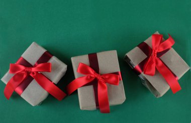 El işi kağıdına sarılı Noel hediyeleri, yeşil bir arka planda el yapımı hediyeler. Noel hediyeleri ve kırmızı Noel yayları. Bayram havasından bir hediye. Yeni yıl Noel dekoru. 