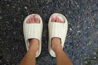  Çimento zemin zemininde açık ayak parmağı yastığı olan bir çift slayt içinde kadın bacakları. Kadın modası. Kadın yaz ayakkabıları, yumuşak terlikler.