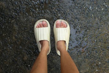  Çimento zemin zemininde açık ayak parmağı yastığı olan bir çift slayt içinde kadın bacakları. Kadın modası. Kadın yaz ayakkabıları, yumuşak terlikler.