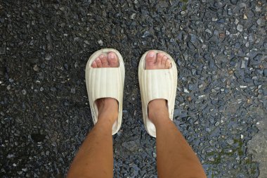  Çimento zemin zemininde açık ayak parmağı yastığı olan bir çift slayt içinde kadın bacakları. Kadın modası. Kadın yaz ayakkabıları, yumuşak terlikler.