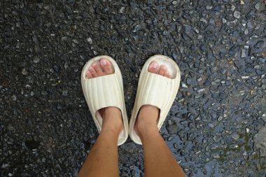  Çimento zemin zemininde açık ayak parmağı yastığı olan bir çift slayt içinde kadın bacakları. Kadın modası. Kadın yaz ayakkabıları, yumuşak terlikler.