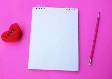 Boş bir defter aç ve dekoratif kırmızı kalp şekli, pembe bir zemin üzerinde pembe bir zemin oluştur. Aşk mesajı, romantik aşk, ofis kırtasiyesi ve Sevgililer Günü tatili kavramı.