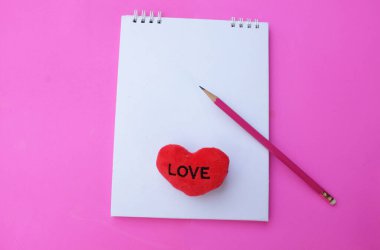 Boş bir defter aç ve dekoratif kırmızı kalp şekli, pembe bir zemin üzerinde pembe bir zemin oluştur. Aşk mesajı, romantik aşk, ofis kırtasiyesi ve Sevgililer Günü tatili kavramı.