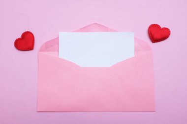 İçinde boş beyaz bir not olan pembe kağıt zarf ve dekoratif kırmızı kalp şekli, pembe pastel arka planda kalem kırmızısı. Mesajın için. Aşk mesajı, Romantik aşk, ofis kırtasiyesi ve Sevgililer Günü 