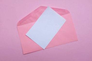 İçinde boş beyaz bir not olan pembe kağıt zarf ve dekoratif kırmızı kalp şekli, pembe pastel arka planda kalem kırmızısı. Mesajın için. Aşk mesajı, Romantik aşk, ofis kırtasiyesi ve Sevgililer Günü 