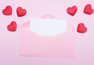 İçinde boş beyaz bir not olan pembe kağıt zarf ve dekoratif kırmızı kalp şekli, pembe pastel arka planda kalem kırmızısı. Mesajın için. Aşk mesajı, Romantik aşk, ofis kırtasiyesi ve Sevgililer Günü 