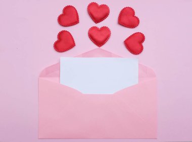İçinde boş beyaz bir not olan pembe kağıt zarf ve dekoratif kırmızı kalp şekli, pembe pastel arka planda kalem kırmızısı. Mesajın için. Aşk mesajı, Romantik aşk, ofis kırtasiyesi ve Sevgililer Günü 