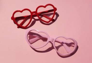 Pembe ve kırmızı güneş gözlükleri, pembe renkli arka planda modern modaya uygun kalp şeklinde. Mesajın için. Aşk mesajı, Aşk romantik, Modern Moda ve Sevgililer Günü kompozisyonu