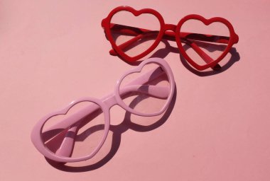 Pembe ve kırmızı güneş gözlükleri, pembe renkli arka planda modern modaya uygun kalp şeklinde. Mesajın için. Aşk mesajı, Aşk romantik, Modern Moda ve Sevgililer Günü kompozisyonu