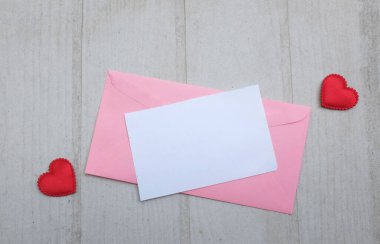 İçinde boş beyaz bir not olan pembe kağıt zarf ve dekoratif kırmızı kalp şekli, Beyaz Tahta Vintage Masa 'da kırmızı kalem. Aşk mesajı, Romantik aşk, ofis kırtasiyesi ve Sevgililer Günü 