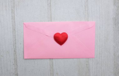 İçinde boş beyaz bir not olan pembe kağıt zarf ve dekoratif kırmızı kalp şekli, Beyaz Tahta Vintage Masa 'da kırmızı kalem. Aşk mesajı, Romantik aşk, ofis kırtasiyesi ve Sevgililer Günü 