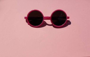 Siyah lensli bir kız için pembe plastik çerçeveli sevimli yuvarlak güneş gözlükleri. Pembe pastel arka planda izole edilmiş. Üst manzara.