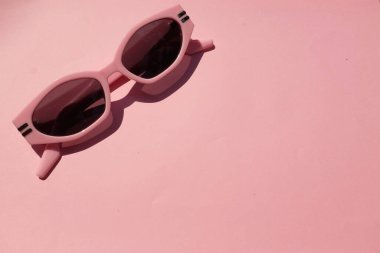 Pembe plastik çerçeveli şirin oval güneş gözlükleri siyah lensli bir kız için pembe pastel arka planda izole edilmiş.